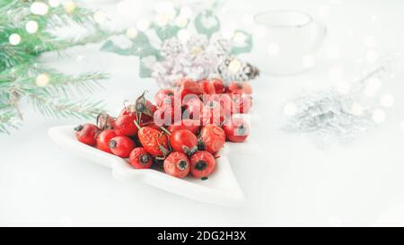 Hagebutte Beeren in einer Porzellanschale in Form eines Weihnachtsbaums auf einem hellen Hintergrund Nahaufnahme. Beeren für die Herstellung von Vitamin-Tee oder trinken auf kalt w Stockfoto