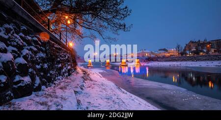 uzhhorod, ukraine - 26 DEC 2016: Winterliche Stadtlandschaft bei Sonnenaufgang. Wunderschöne Landschaft an der uzh. Lichter der Stadt spiegeln sich im Wasser. Schnee am Ufer Stockfoto