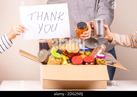 Freiwillige sammeln Lebensmittel zu Lebensmittel Spende Box und halten Papierbogen mit Nachricht Vielen Dank Stockfoto