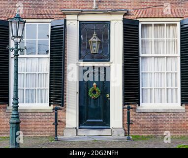 Weihnachtsterrasse. Hausfassade mit Vintage-Eingangstür mit weihnachtskranz und antiken Fensterläden dekoriert. Schwarze Vintage-Tür mit festlichen Stockfoto