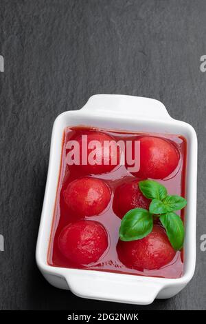 Hausgemachte geschälte Tomaten in Tomatensaft in Keramikschale auf Schwarzer Stein Hintergrund Stockfoto