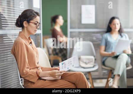 Seitenansicht Porträt der eleganten jungen Geschäftsfrau Blick auf Charts und Bericht während der Wartezeit in der Schlange im Büro, Platz kopieren Stockfoto