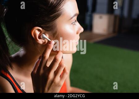 Junge Sportlerin, die schnurlose Kopfhörer anfasst und beim Sport wegschaut Zentrieren Stockfoto