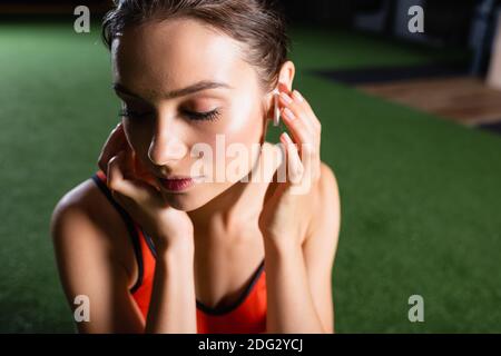 Die junge Sportlerin berührt den kabellosen Kopfhörer, während sie im Fitnessstudio Musik hört Stockfoto