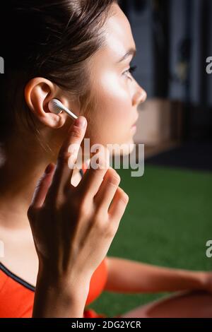 Sportlerin, die wegschaut, während sie im Fitnessstudio den kabellosen Kopfhörer berührt Stockfoto