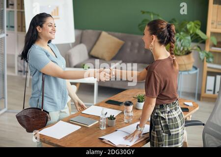 Portrait von zwei jungen Frauen, die nach einem erfolgreichen Vorstellungsgespräch die Hände über den Tisch schüttelten, Platz kopieren Stockfoto