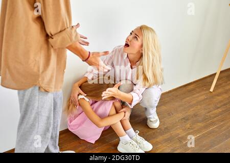 Eine Frau sitzt mit einem Kind, beruhigt sie, während ein Mann schwört auf sie. Kleines Mädchen ist aufgebracht deprimiert über das Verhalten des Vaters Stockfoto