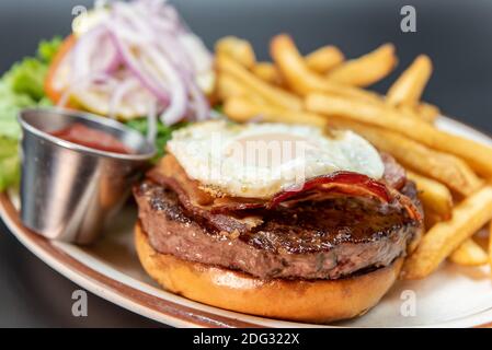 Frisch vom Grill gebratenes Ei, Speck und Hamburger mit allen bekannten pommes Frites und vegetarischen Beilagen. Stockfoto