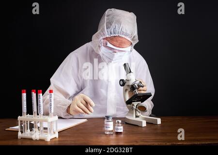 Arzt machen Forschung mit Blutschlauch für Covid-19 oder nCoV Coronavirus-Test, Tragen Schutzanzug isoliert über schwarzem Hintergrund Stockfoto