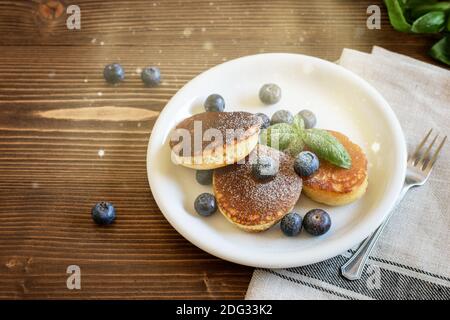 Heiße traditionelle Pfannkuchen mit Heidelbeeren auf dem weißen Teller. Pfannkuchen mit Zuckerpulver, Soft-Motion-Foto, Draufsicht. Stockfoto