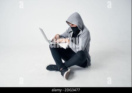 Ein Mann in einer Maske sitzt auf dem Boden innen Vor einem Laptop-Computer Hacking Verbrechen Stockfoto