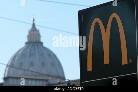 Ein Schild, das die Richtung eines neu eröffneten McDonald's Restaurants zeigt, ist am 4. Januar 2017 in Rom, Italien, mit der Kuppel der Petersbasilika im Hintergrund in der Nähe des Vatikans zu sehen. Die amerikanische Fast-Food-Kette eröffnete ein Restaurant in einem Gebäude im Besitz des Vatikans, trotz des Protests eines Komitees zum Schutz von Borgo, dem historischen Viertel rund um den Vatikan, in dem viele Kardinäle leben. Trotz einer sehr öffentlichen Schlacht von Einheimischen und religiösen Beamten, um die Fast-Food-Kette aus dem päpstlichen Hauptquartier zu halten, öffnete eine Filiale der Golden Arches Kette Restaurant für Geschäfte nur wenige Meter entfernt Fr. Stockfoto