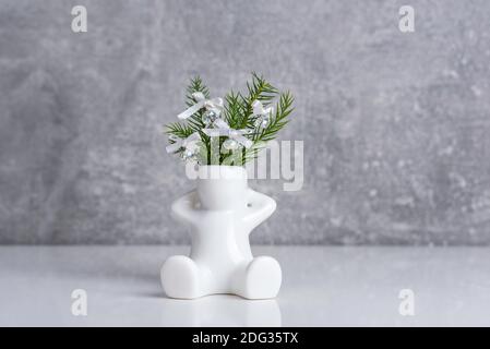 Kleine weiße Keramikvase - Figur des Menschen mit Araucaria Pflanzenzweige mit Glasperlen und Band Bögen verziert. Miniatur-Weihnachtsdesign. Stockfoto