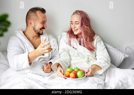 Paar essen Früchte auf dem Bett, liebenswert Frau und Mann genießen Sie das Essen am Morgen auf dem Bett liegen, in Hausbademäntel. Entspannen, Urlaub, Ruhe Stockfoto