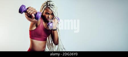 Nahaufnahme einer fitten afroamerikanerin, die mit Hanteln Stanzübungen macht. Fitness-Frau, die am Training der Armmuskulatur arbeitet. Stockfoto