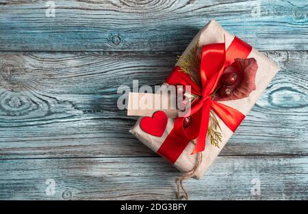 Geschenkbox mit rotem Band, Beeren und einem Herzen auf einem natürlichen grau-blauen Holzhintergrund dekoriert. Stockfoto