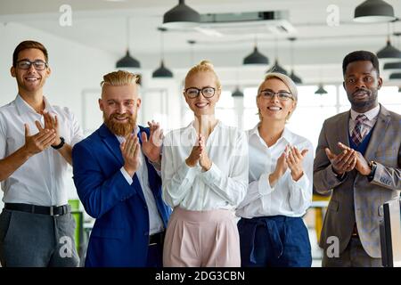 Glückliches Geschäftsteam gratuliert Kollegen mit einem guten Job für das erfolgreiche Projekt, Blick auf die Kamera lächelnd und klatschende Hände Stockfoto