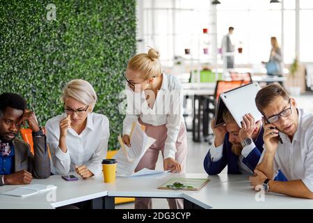 Wütende Chefin schimpft die Angestellten am Ende des Monats wegen eines schlechten Ergebnisses, schreit und schreit im Büro, diverse Arbeiter sitzen in Angst vor ihr Stockfoto