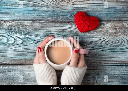 Hände einer Frau, die eine Tasse Kaffee mit Milch auf einem romantischen Hintergrund hält. Stockfoto