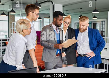 Multi-ethnisch freundliches Team von Kollegen reden Projekte diskutieren, schwarze Männer halten Papier in den Händen, geben Anweisungen Stockfoto