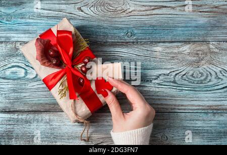 Die Hand einer Frau schmückt das Herz einer Geschenkbox auf einem Holzhintergrund. Stockfoto