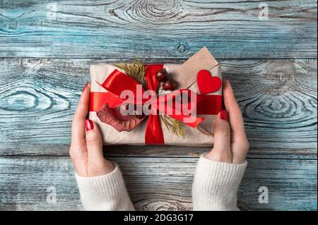 Geschenk mit rotem Band in Damenhänden auf Holzhintergrund. Stockfoto