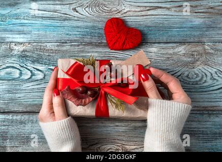 Damenhänden schmücken eine Geschenkbox auf einem Holzhintergrund. Stockfoto