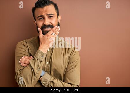 Trauriger arabischer Mann, der Gesicht isoliert hält, sich schlecht fühlt, mit enttäuschtem Gesicht isoliert auf braunem Hintergrund Stockfoto