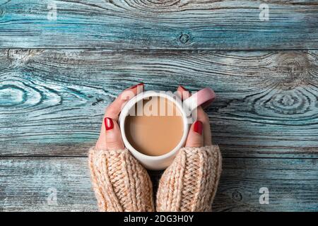 Damenhänden halten eine runde Keramikschale mit einem heißen Kaffeegetränk auf einem hölzernen Hintergrund. Stockfoto