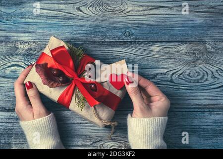 Festlicher Hintergrund mit einer Geschenkbox und Damenhänden auf einem grau-blauen Holzhintergrund. Stockfoto