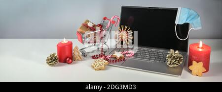 Urlaub Online-Shopping während Coronavirus Pandemie, Laptop, chirurgische Gesichtsmaske gegen covid-19 Pandemie, brennende Kerzen, Weihnachtsdekoration und Stockfoto