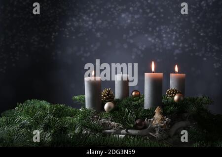 Drittes Advent mit drei brennenden Kerzen auf Tannenzweigen mit Weihnachtsdekoration vor dunkelgrauem Hintergrund, Kopierraum, ausgewählter Fokus, schmal d Stockfoto