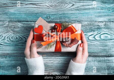 Geschenkbox in den Händen einer Frau auf einem grau-blauen Holzhintergrund. Stockfoto
