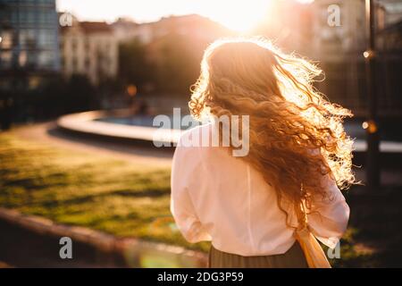 Rückansicht einer Frau mit zerzausten Haaren, die in der Stadt steht Bei Sonnenuntergang Stockfoto