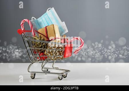 Warenkorb-Modell mit Geschenk, weihnachtsdekoration, Süßigkeiten und einer chirurgischen Gesichtsmaske gegen Coronavirus-Infektion, sichere Urlaub Einkäufe während der Stockfoto