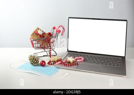 Online-Shopping für Weihnachten während der Coronavirus-Pandemie, Laptop-Modell mit weißem Monitor, chirurgische Gesichtsmaske gegen covid-19 Pandemie und ein smal Stockfoto