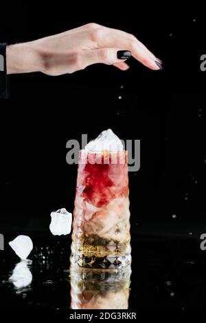 Heller alkoholischer Cocktail auf schwarzem Hintergrund und einer Frau Hand mit fallendem Eis Stockfoto