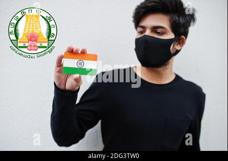 Indische Mann tragen alle schwarzen und Gesichtsmaske, halten Indien Flagge in der Hand isoliert auf weißem Hintergrund mit Tamil Nadu Staatswappen . Coronavirus Indien Staaten Stockfoto