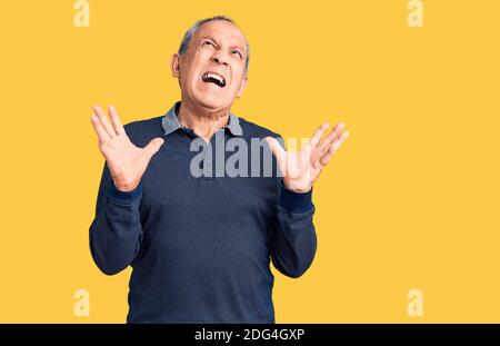 Senior schöner Mann trägt Casual Polo verrückt und verrückt schreien und mit aggressivem Ausdruck und Arme angehoben. Frustration Konzept. Stockfoto