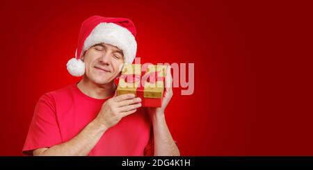 Mann in Santa Hut erhalten Weihnachtsgeschenk, hält in der Nähe seines Gesichts und lächelnd Stockfoto