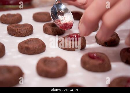 Hand der Frau hält EINEN Löffel und setzt Cherry Jam hinein Schokoladenteig, Um Weihnachtsplätzchen Zu Machen Stockfoto