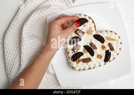 Schritt-für-Schritt-Rezept für herzförmige Kuchen. Schritt 12: Den Kuchen mit Schokoladenstückchen, Waffeln, Keksen dekorieren. Flach liegend. Stockfoto