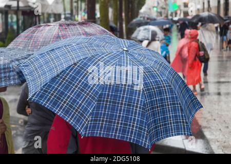 Menschen mit Sonnenschirmen unterwegs in der Regenstadt Stockfoto