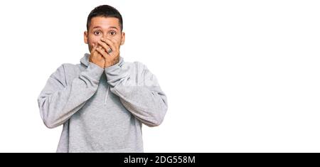 Schöner Mann mit Tätowierungen tragen lässige Sweatshirt schockiert Abdeckung Mund mit Händen für Fehler. Secret Konzept. Stockfoto