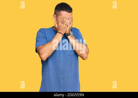 Schöner Mann mit Tätowierungen tragen Freizeitkleidung mit trauriger Ausdruck bedeckt Gesicht mit Händen beim Weinen. Depression Konzept. Stockfoto