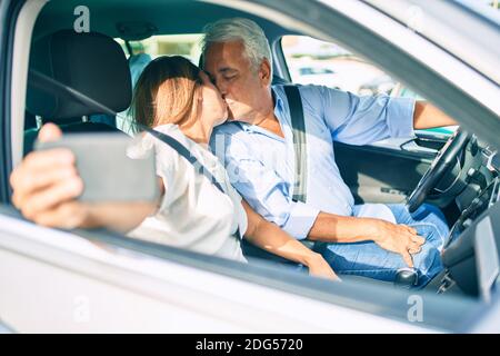 Mittelalterpaar verliebt sitzt im Auto gehen Für eine Reise ein Selfie-Foto mit Smartphone küssen Stockfoto