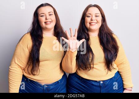 Junge Zwillinge in lässiger Kleidung zeigen und zeigen mit den Fingern Nummer fünf, während sie selbstbewusst und glücklich lächeln. Stockfoto