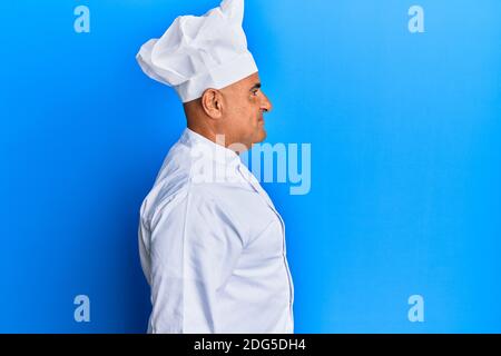 Reifer Mann aus dem Nahen Osten trägt professionelle Koch Uniform und Hut suchen zur Seite, entspannen Profil Pose mit natürlichen Gesicht mit selbstbewussten Lächeln. Stockfoto