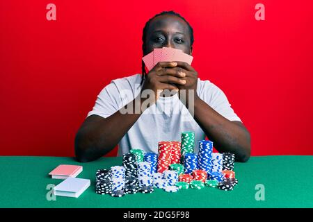 Schöner junger schwarzer Mann spielen Glücksspiel Poker Bedecken Gesicht mit Karten ragen Zunge aus glücklich mit lustigen Ausdruck. Stockfoto