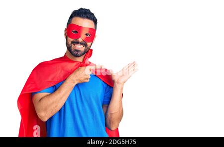 Junge hispanic Mann trägt Superhelden Kostüm erstaunt und lächelt an der Kamera, während mit der Hand und zeigt mit Finger. Stockfoto